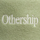Closeup of the white embroidered “Othership” logo on the green felt sauna hat.