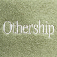 Closeup of the white embroidered “Othership” logo on the green felt sauna hat.